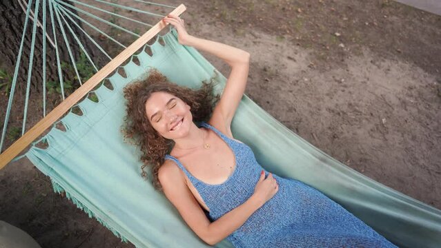 Curly girl lies in a blue hammock in a blue dress