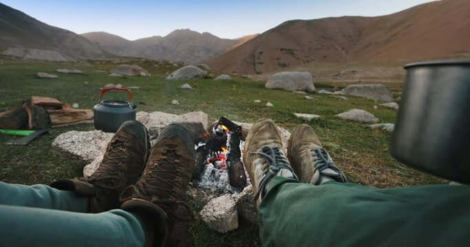 Legs of travelers campers by fire. Hikers warm by burning fire early in morning drink coffee tea warm feet legs by fire start day gain strength before active day full of tourist adventure in mountains