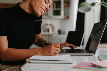 Close-up of happy young woman talking on mobile phone and making notes while working at home