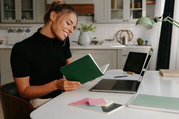 Busy young woman talking on mobile phone and looking at the note pad while working at home