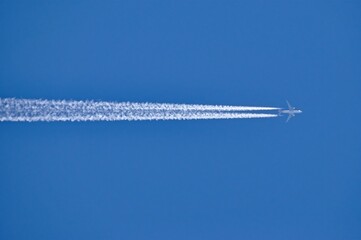 A twin-engine passenger plane in flight at high altitude and the white contrail it leaves behind,...