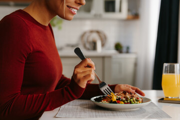 Close-up side view of young woman enjoying healthy food for lunch at the domestic kitchen