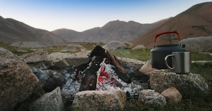 Burning campfire in morning. Sunrise in mountains in hilly terrain fire burned all night and warms sleeping campers burns out at dawn. Morning at tourist hiker camp in mountains hills with campfire