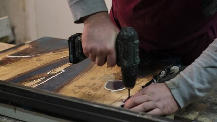 A focused craftsman drills into wood, hands steady and determined. Captures the dedication behind handmade furniture creation.