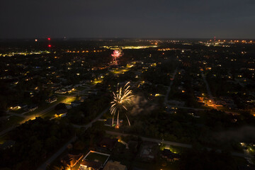 Aerial view of bright fireworks exploding with colorful lights over suburban houses in residential area on US Independence day holiday