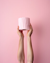 two outstretched hands carries a roll of toilet paper isolated on a pink background, the essential for confinement