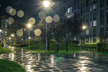 Night park paths and colored houses on a rainy autumn night. Night paths, benches, lanterns in a beautiful residential complex. Night autumn park with lanterns, benches, yellow leaves. Kyiv. Ukraine - obrazy, fototapety, plakaty