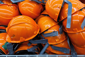 Many orange construction helmets lie on top of each other in a pile. Construction safety worker...