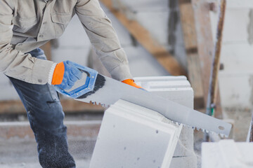 Sawing an autoclaved aerated block with a hand saw at a construction site.