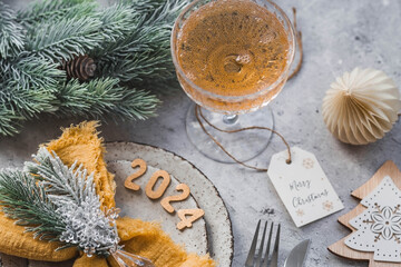 Table setting. Stylish plates, napkin, glass, champagne, Christmas tree branches and Christmas decorations on a gray background. The concept of merry Christmas and New Year 2024.