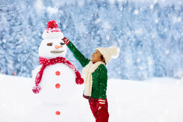 Child building snowman. Kids build snow man.