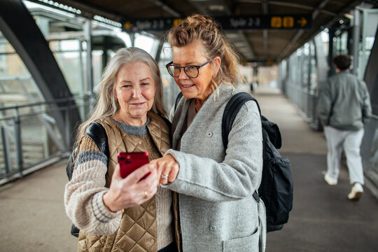 Two senior women looking at smartphone pointing in train station