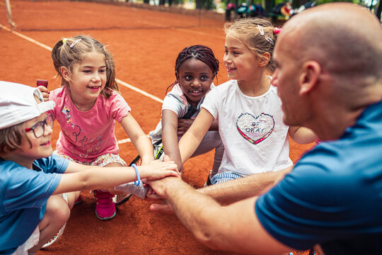 Children and their coach come together in a huddle on the tennis court - Powered by Adobe