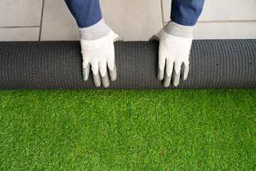 Men's hands holding a roll of artificial grass and installing it on a house. Artificial grass...