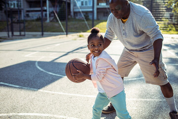 Adorable little girl playing basketball with father on outdoor court