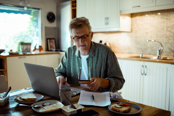 Mature man holding credit card using laptop