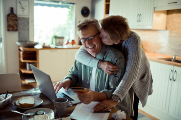 Mature middle aged senior couple online shopping from laptop at home