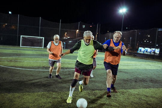 Active Elderly Men Playing Football Under Floodlights