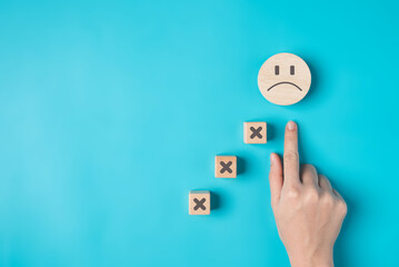 Unhappy face on wooden block of customer feedback review, Hand with sad face icon on background, Bad feeling and poor service, Dissatisfied client expressing, Negative feedback survey