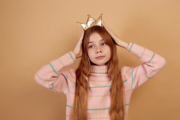 Little cute girl holding golden crown by hands on beige background.