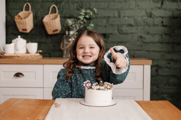 Adorable little child girl wears festive dress takes a bite out of a decorated flowers name cake at...