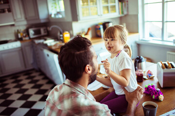 Fototapeta premium Father and Daughter Playing with Food in the Kitchen. Little girl putting chocolate on dad face being messy concept