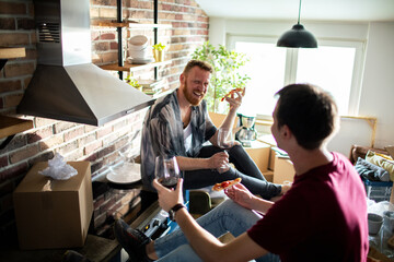 Young gay male couple eating and having wine in new kitchen - obrazy, fototapety, plakaty