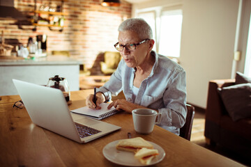 Senior woman working from home and taking notes