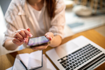 Woman working on a laptop in her kitchen while checking her smartphone