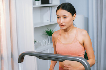 Energetic and strong athletic asian woman running running machine at home. Pursuit of fit physique...