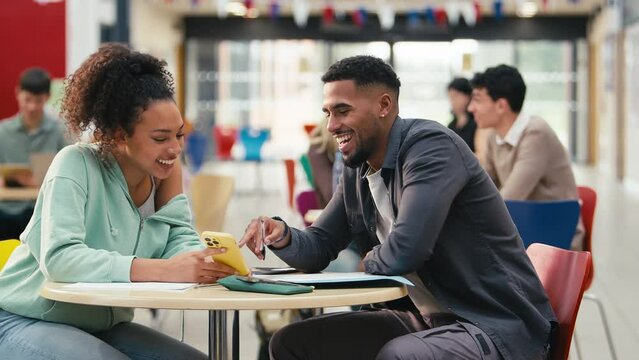 Two college or university students looking at mobile phone working together in study area - shot in slow motion