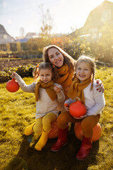 Mom and little daughters laughing in autumn in rain boots with pumpkins