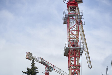 Tower cranes near a building under construction against the background of the sky and white clouds. Construction concept. With space to copy. High quality photo