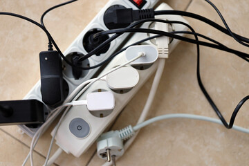 Overloaded power boards. Power strips with different electrical plugs on white floor. Concept of...