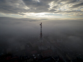 communications tower in the mist during sunrise over cloud-covered city