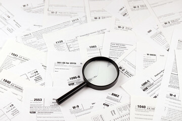 Magnifying glass lying over heap of paper documents. Investigation and financial audit concept