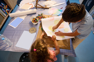 View from above of inspired children learning art, drawing with pencils in creative workshop. Elementary age school.