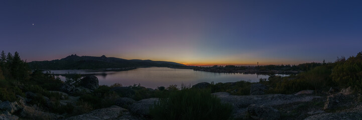 Fototapeta premium Panorama of evening twilight with Crescent moon over mountain lake after sunset in rocky pure landscape, Vale do Rossim, Serra da Estrela, Portugal