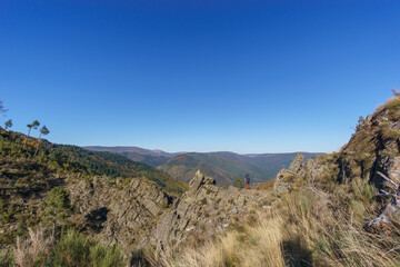 Hikers view over mountain landscape with autumn colored forest over the famous waterfall called Poco do Inferno, Manteigas, Serra da Estrela, Portugal