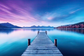  a dock that is sitting in the middle of a body of water with a mountain range in the background and clouds in the sky.