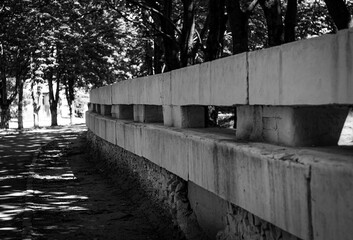 Black and white photo of a concrete fence on a sunny day in a park among trees.