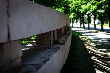 A color photo of a concrete fence on a sunny day in a park among trees.