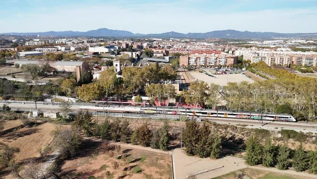 Trenes Renfe R2 Rodalies entrando y saliendo de la estaci&oacute;n de Santa Perp&egrave;tua de Mogoda, con vistas a Montserrat y al lago de Parc Central y un partido de f&uacute;tbol, grabado desde dron 4k 60fps.