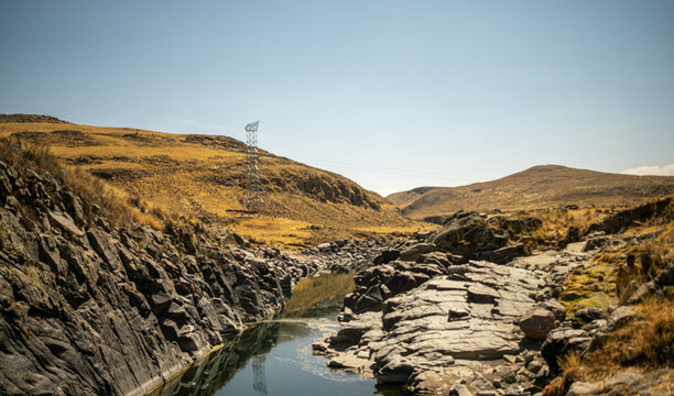 
River near rock with yellow landscape, distant mountains and blue sky in the background in Espinar, Cusco, Peru.