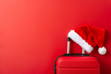 Explore the Winter Getaway idea. Overhead shot of stylish suitcase, and a Santa Claus hat, all on a vibrant red backdrop with space for text
