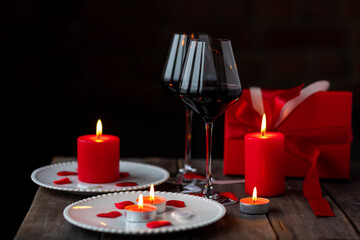 Saint Valentine's Day celebration. Red burning candles, hearts, gift box, postcard on dark wooden background. Happy holiday . Table decor for festive dinner, romantic atmosphere. Copy space for text