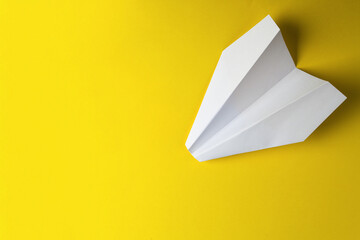Flat lay of white paper plane on pastel yellow color background