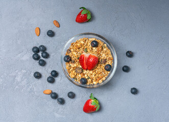 Granola in a glass bowl with strawberries, blueberries, raisins and nuts on a concrete table. View from above.