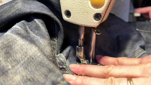 Sewing work. Stitching a hole in jeans with a sewing machine. Seamstress sews with jeans cloth. Darning jeans on a sewing machine. Seamstress sews on a sewing machine. Tailoring.