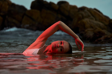 Woman swims in serene lagoon at dusk, reflective water surrounds her, tranquil aquatic leisure...